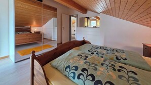 Une chambre avec un plafond en bois, un lit avec une literie à motifs, une table de chevet et un miroir.