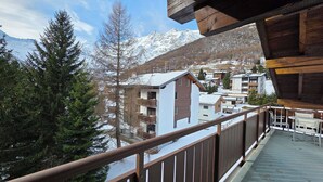 Un balcon offrant une vue sur un paysage montagneux enneigé, avec des balustrades en bois et une table entourée de chaises.