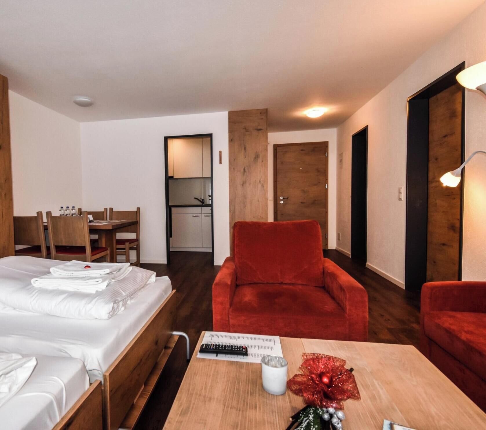 Une chambre d’hôtel avec un lit, un bureau, une chaise rouge et une petite table sur laquelle se trouvent une télécommande et un objet décoratif.