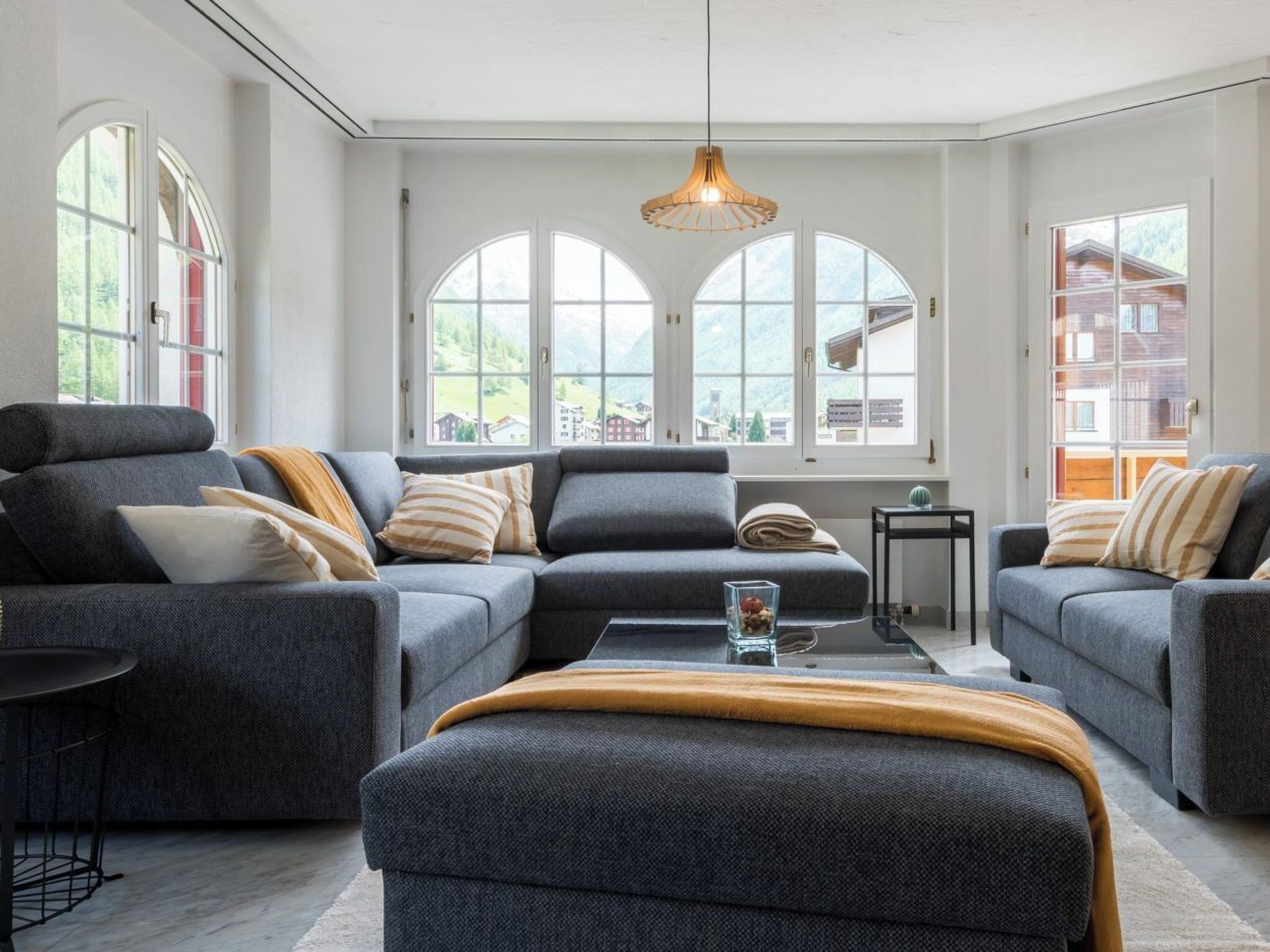Un salon moderne avec un canapé d’angle, une table basse et de grandes fenêtres donnant sur un paysage montagneux.