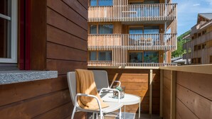 Een houten balkon met een witte metalen stoel en tafel, een raam en uitzicht op een meer verdiepingen tellend gebouw.