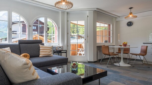 Een moderne woonkamer met een bank, salontafel en een eethoek met stoelen.