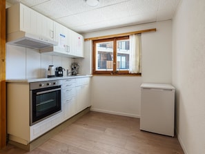 Eine kompakte Küche mit weißen Schränken, einem eingebauten Backofen, einer Kaffeemaschine und einem Fenster mit Vorhängen.