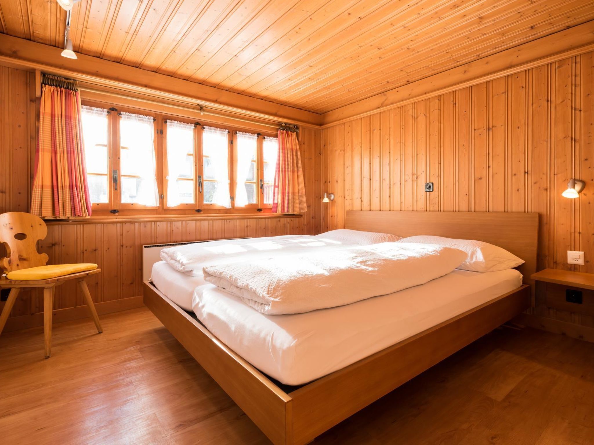 Ein Zimmer mit Holzwandverkleidung, einem Bett, einem Sessel und einem Fenster mit Vorhängen.