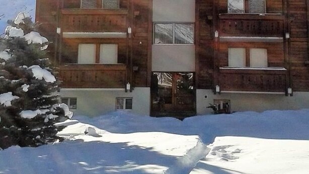Una cabaña de madera con un cartel que dice 'Aster' frente a una montaña nevada.