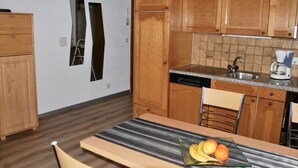 Cocina compacta con armarios de madera, lavavajillas, cafetera y una mesa de comedor con sillas.