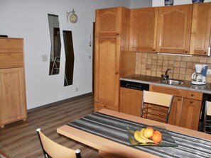 A compact kitchen with wooden cabinets, a dishwasher, a coffee maker, and a dining table with chairs. - Aster Appartement/Fewo, Bad, WC, 2 Schlafräume 4-Bettwohnung by Interhome (Saas-Fee)