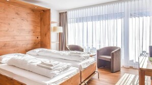 Ett hotellrum med två sängar, en garderob i trä, ett skrivbord med en stol och ett stort fönster med gardiner.