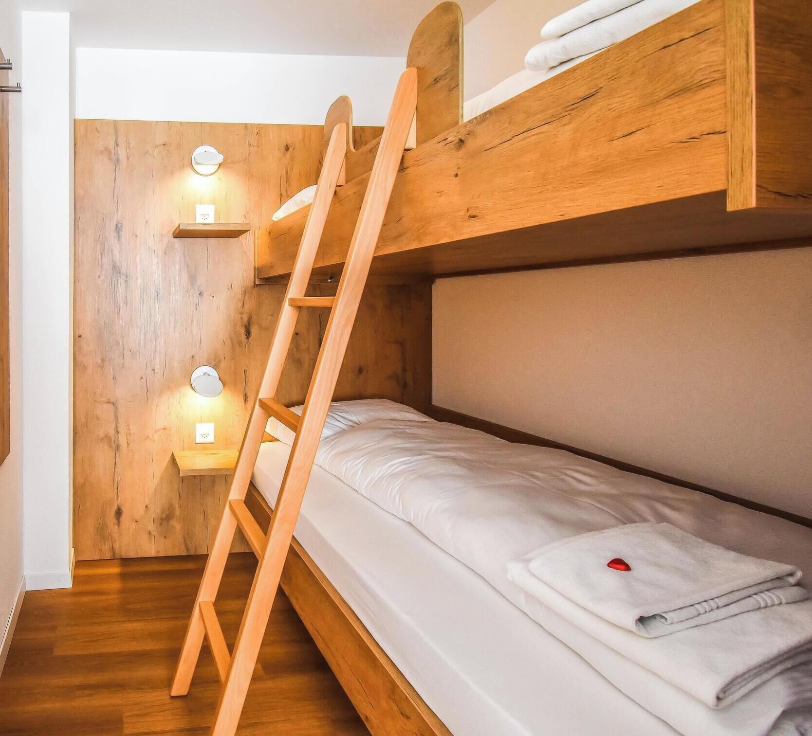 Een stapelbed met een houten ladder, een klein plankje en twee wandlampen.