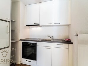 Eine kompakte Küche mit weißen Schränken, einem Backofen, einer Spüle und einem Kühlschrank.