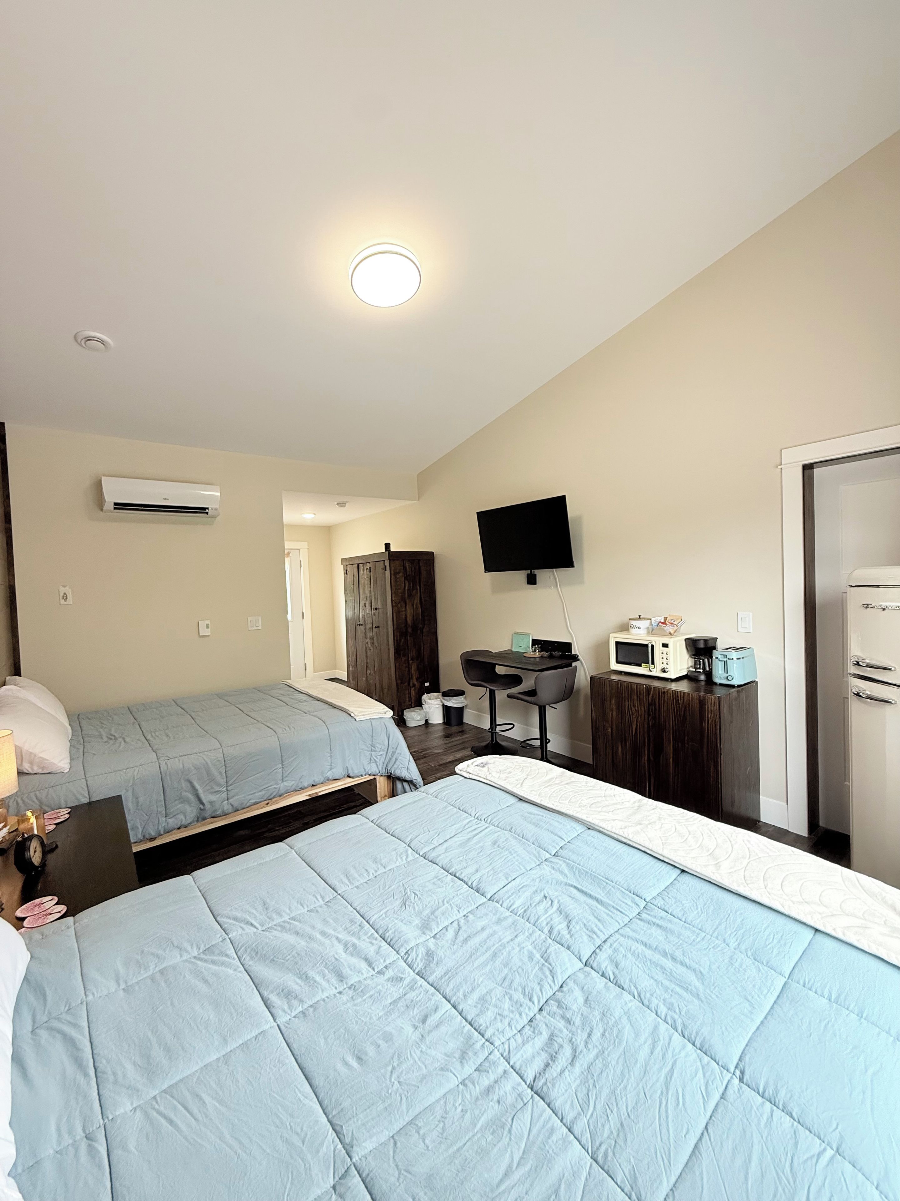 Ein Hotelzimmer mit zwei Betten, einem Schreibtisch mit Stuhl, einem Fernseher und einer Küchenzeile.