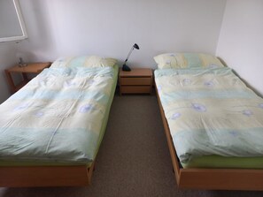 Ein Doppelzimmer mit zwei Einzelbetten, einem Nachttisch mit Lampe und einer kleinen Holzkommode.