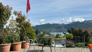 Un patio con dos sillas y una mesa, con vistas a un lago y montañas.