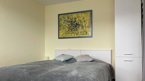 Un dormitorio con cama, almohadas, un armario blanco y un cuadro en la pared.