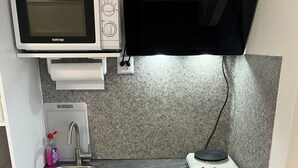 Una cocina compacta con microondas, un lavamanos, un refrigerador pequeño y una balanza.