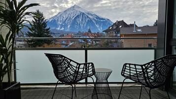 Un balcon avec deux chaises et une petite table, d’où l’on peut admirer une montagne et des immeubles d’habitation.
