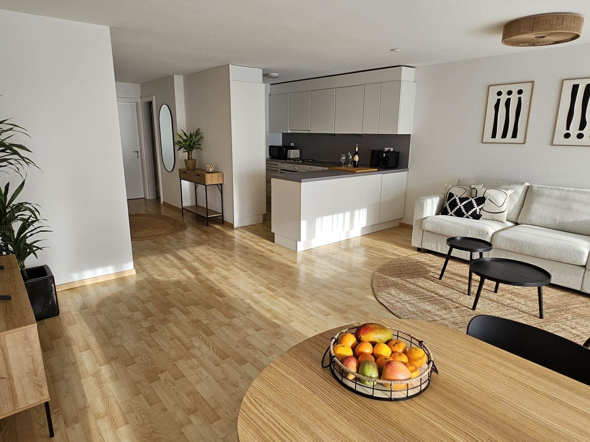 Une cuisine moderne avec des meubles blancs, un coin repas doté d’une table ronde en bois et un salon avec un canapé et une table basse.