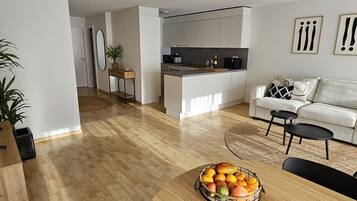 Une cuisine moderne avec des meubles blancs, un coin repas doté d’une table ronde en bois et un salon avec un canapé et une table basse.