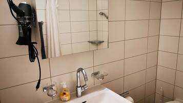 A bathroom with a sink, mirror, hairdryer, and shower.