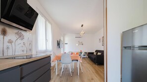 Eine moderne Küche mit integriertem Fernseher, ein Essbereich mit Tisch und Stühlen, eine Couch und ein Kühlschrank.