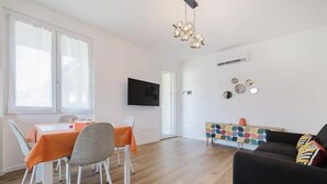 A modern living room with a dining area, a sofa, a TV mounted on the wall, and a colorful sideboard. - Red Maple - Immobiliare Azzurra (Bardolino)