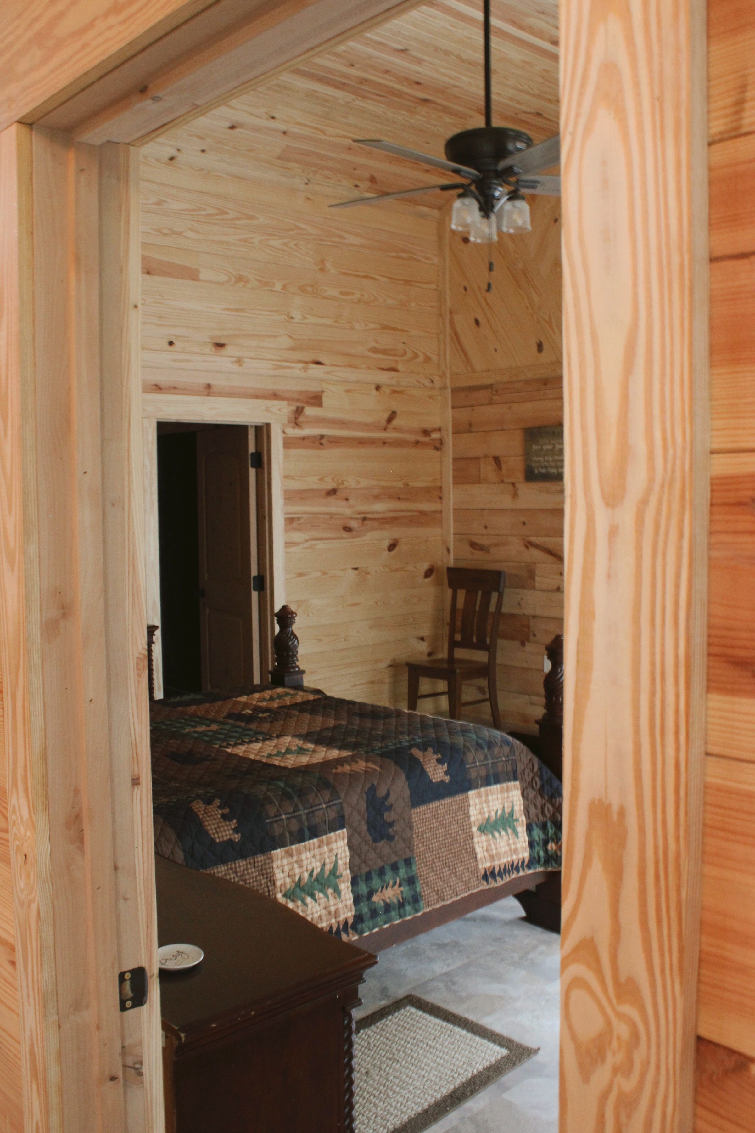 A wooden-paneled room with a bed, a chair, and a desk.