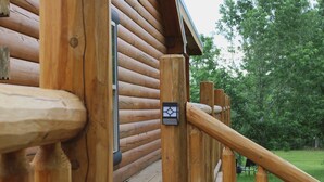 A wooden log cabin with a wooden deck and a metal railing. - Rustic and Elegant Creekside Log Cabin (Wing)
