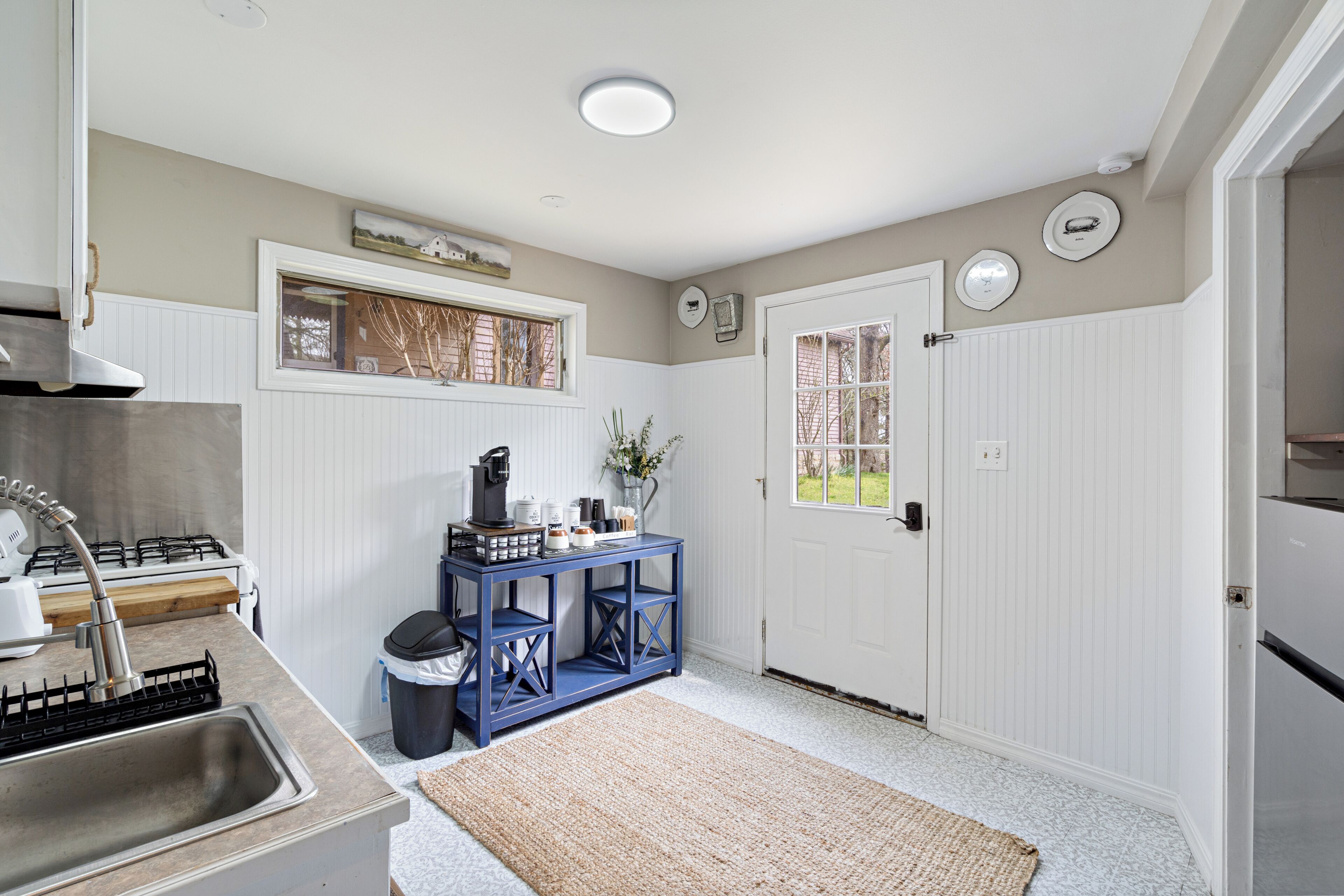 A kitchen with a gas stove, sink, blue console table, and a window with a view.