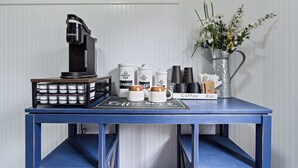 Una cafetería con una máquina Keurig, tazas de café, recipientes de azúcar y leche, un jarrón con flores y un letrero que dice 'Coffee Bar'.