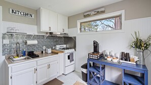 Una cocina con armarios blancos, estufa, fregadero y una barra para café azul.