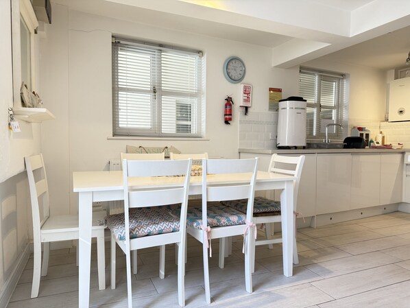Un comedor con una mesa y sillas, una cocina con refrigerador y estufa, y un extintor en la pared.