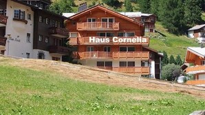 Ein mehrgeschossiges Gebäude mit Balkonen, mit dem Schriftzug 'Haus Cornelia', vor einer bewaldeten Hügelkulisse.