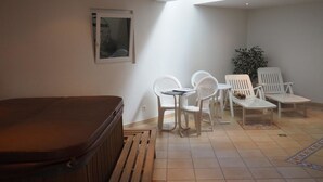 Ein Zimmer mit Whirlpool, weißen Plastikstühlen, einem kleinen Tisch und einer Topfpflanze.