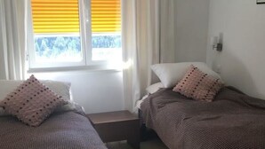 Ein Schlafzimmer mit zwei Betten, einem Fenster mit Jalousien, einem Teppich und einer Wandleuchte.