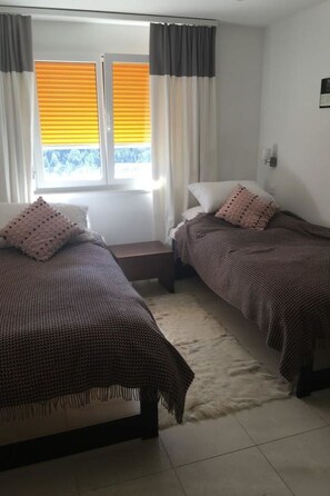 Ein Schlafzimmer mit zwei Betten, einem Fenster mit Jalousien, einem Teppich und einer Wandleuchte.