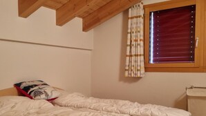 A bedroom with a single bed, a window with blinds, a wooden ceiling, and a small bedside table. - Snow-Fun B Penthouse Appartement/Fewo Appartement/Fewo by Interhome (Saas-Fee)