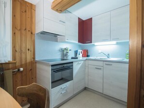 A compact kitchen with white cabinets, a red accent wall, a built-in oven, and a sink. - Chalet Alpenruh Appartement/Fewo Nr. 3 Mischabel by Interhome (Saas-Fee)