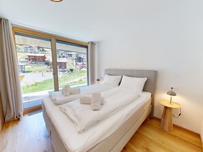 Ein Hotelzimmer mit einem großen Bett, einem Nachttisch mit Lampe und Blick auf Gebäude durch ein großes Fenster.