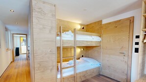 Een kamer met een stapelbed, houten wanden, een deur met een greep en een klein tafeltje.