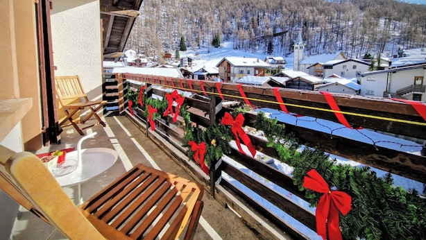 Un balcon avec des balustrades en bois, une chaise en bois et une vue sur une montagne enneigée et un village.