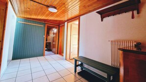 Un couloir avec un plafond en bois et un sol carrelé, qui mène à une pièce où se trouvent un banc et un radiateur.