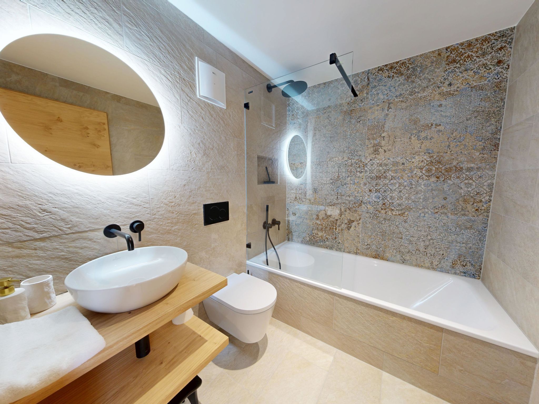 A modern bathroom with a large oval mirror, a white sink, a toilet, and a bathtub.