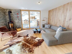 A modern living room with a stone wall, a fireplace, a sofa, and a large window. - Alphubel Peak & Unlimited Appartement/Fewo Peak 07 by Interhome (Saas-Fee)
