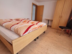 Un dormitorio con cama, una silla, armario y una mesita.