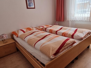 A double bed with striped bedding, a bedside table with a lamp, and a window with curtains. - Orion Appartement/Fewo 4-Bettwohnung Nr. 54 by Interhome (Saas-Grund)