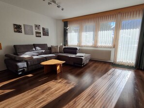 Una sala de estar con un sofá modular, una mesa de centro de madera y un ventanal con cortinas.