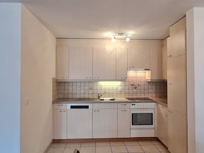 A compact kitchen with light-colored cabinets, a built-in dishwasher, a stove, and a sink. - Orion Appartement/Fewo 4-Bettwohnung Nr. 54 by Interhome (Saas-Grund)