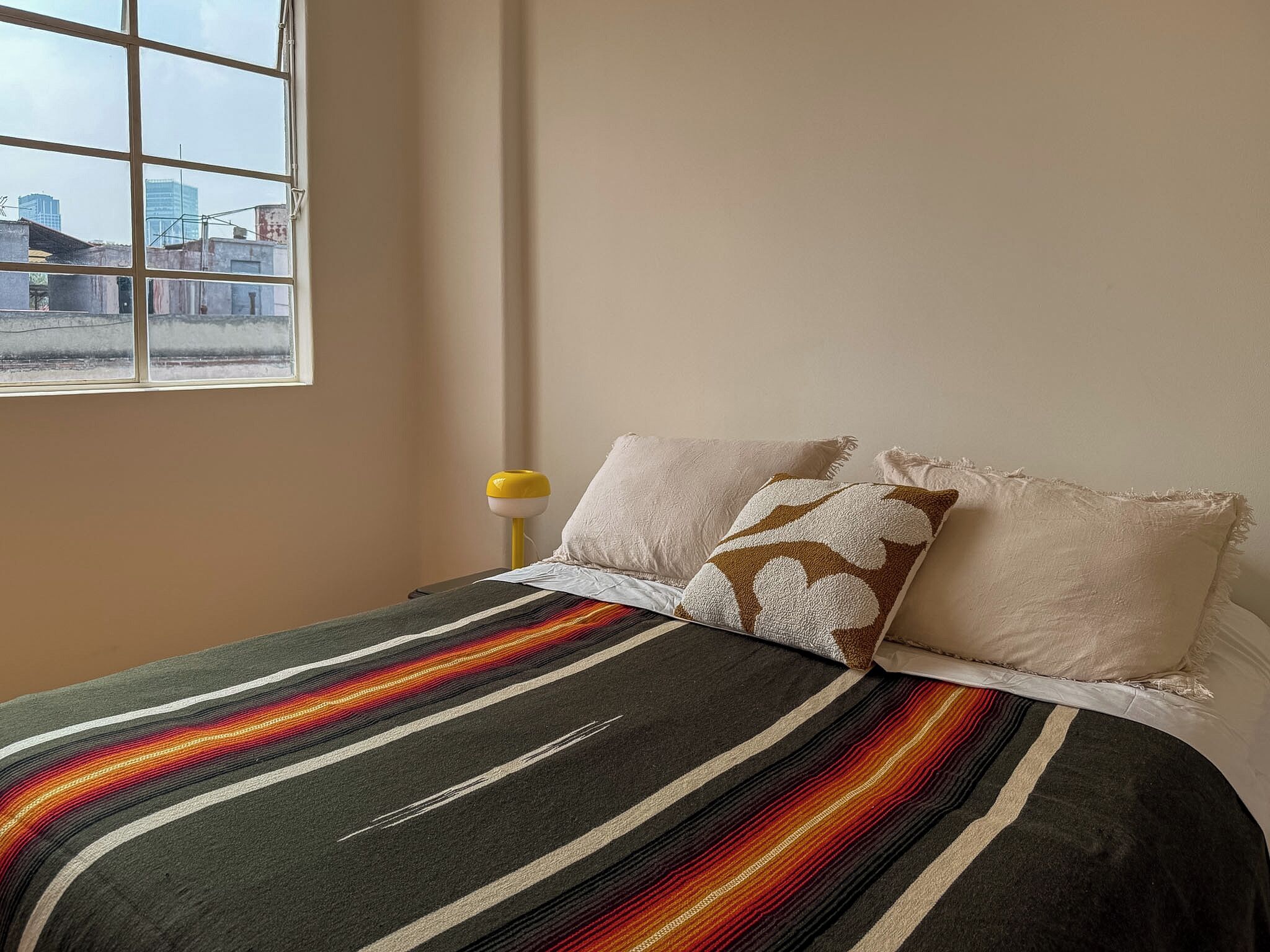 A bedroom with a bed, pillows, a window, and a lamp.