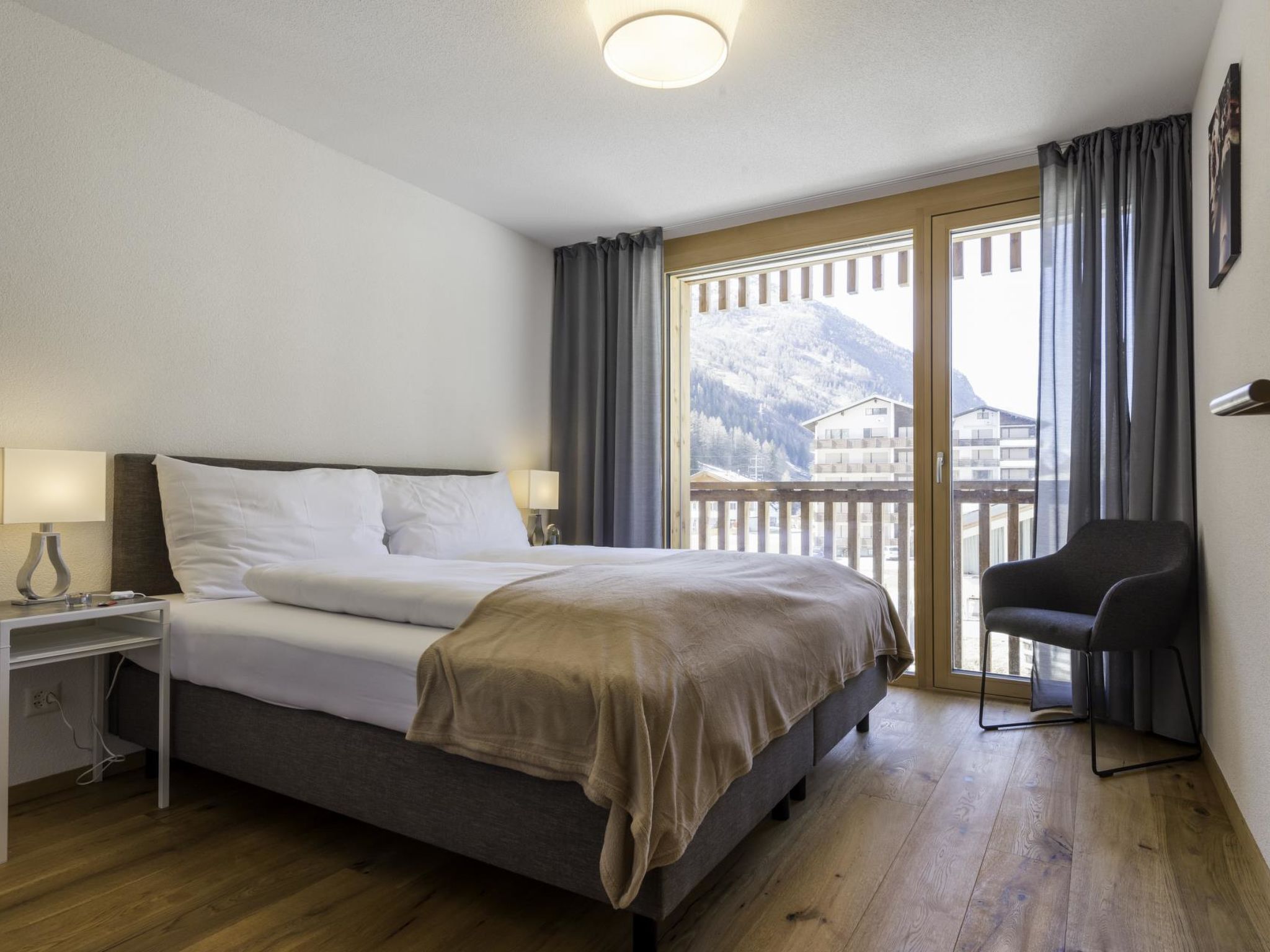 Une chambre d’hôtel avec un lit, une table de chevet, une chaise et une vue sur une montagne.