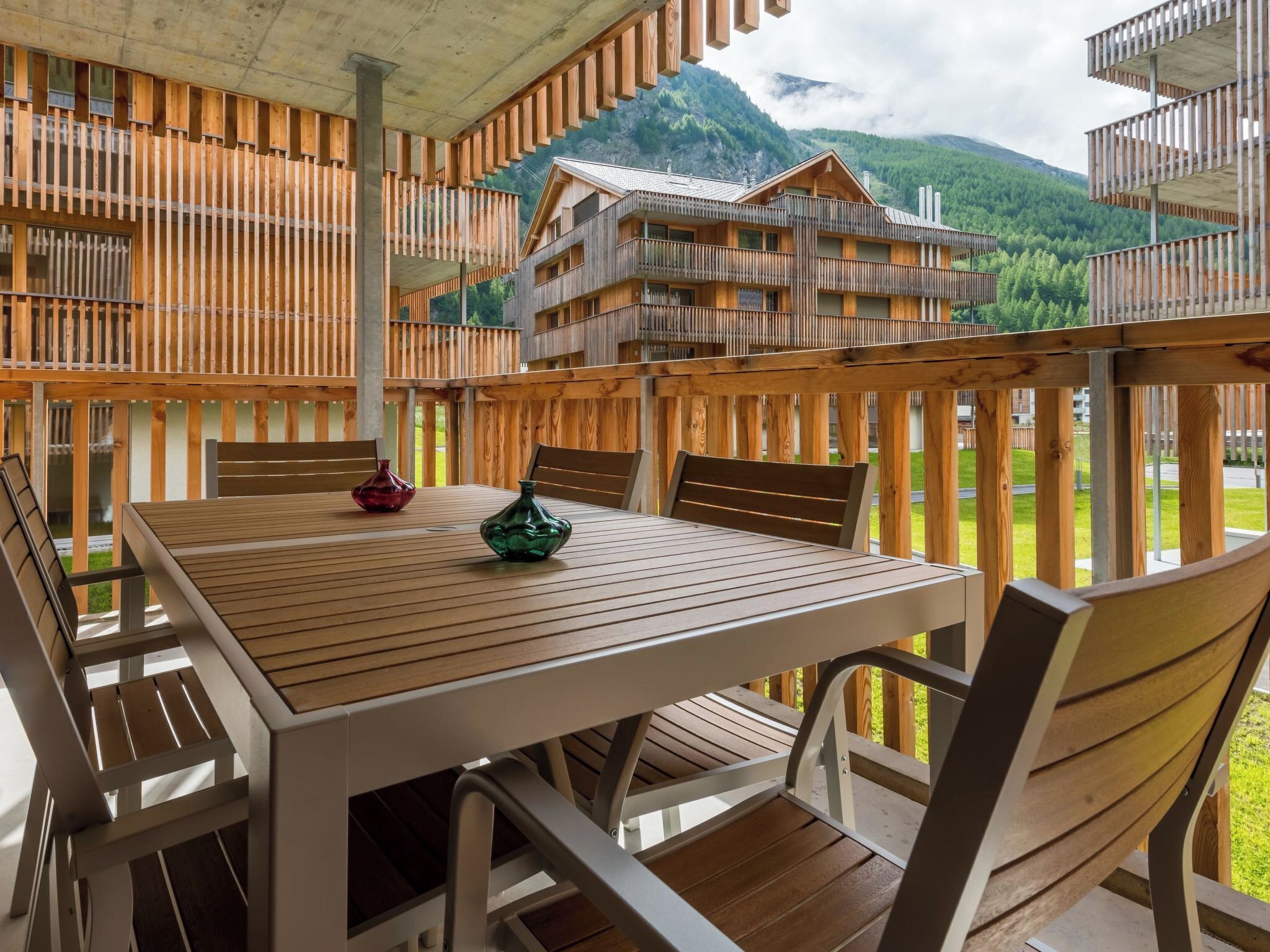 Una terraza de madera con mesa y sillas, con vistas a un paisaje montañoso.